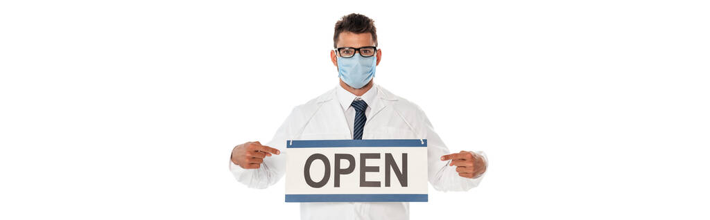 Панорамний урожай лікаря в медичній масці, що вказує пальцями на вивіску з відкритим написом ізольовано на білому
 - Фото, зображення