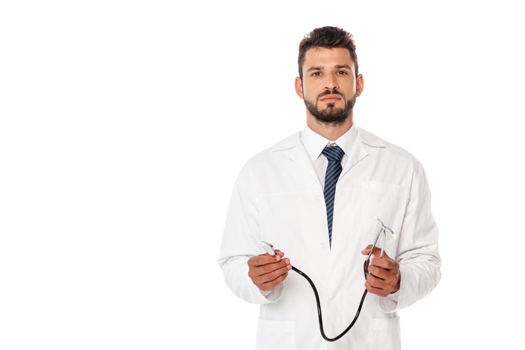 Schöner Arzt blickt auf Kamera und hält Stethoskop isoliert auf weiß - Foto, Bild