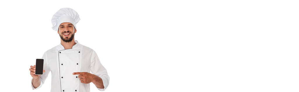 Foto panoramica di chef sorridente che punta con il dito lo smartphone isolato sul bianco - Foto, immagini