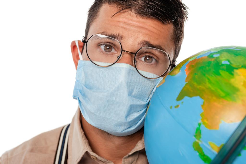 Foco seletivo de nerd em máscara médica segurando globo e olhando para a câmera isolada no branco
 - Foto, Imagem