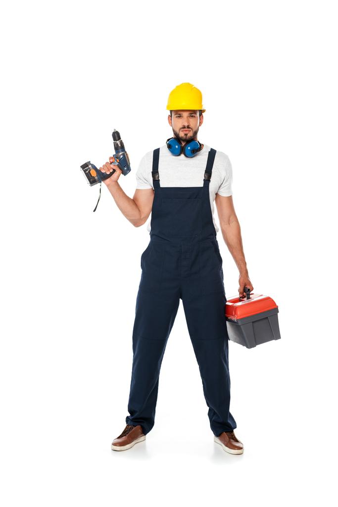Schöner Arbeiter in Uniform und mit festem Griff zu Elektroschrauber und Werkzeugkiste auf weißem Hintergrund - Foto, Bild