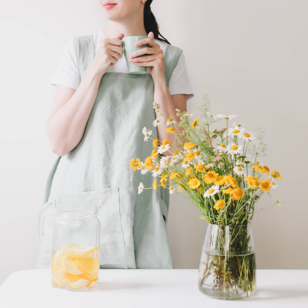 Donna in lino grembiule bere limonata con accogliente sfondo casa. Grembiule in tessuto naturale pulito. Food blogger, cucina casalinga - Foto, immagini