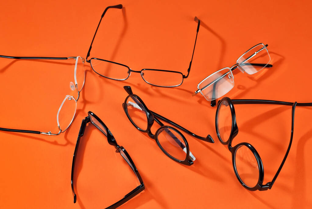 Różne rodzaje okularów na pomarańczowym tle z bliska. Szklanki z prostokątnymi i okrągłymi ramami. - Zdjęcie, obraz
