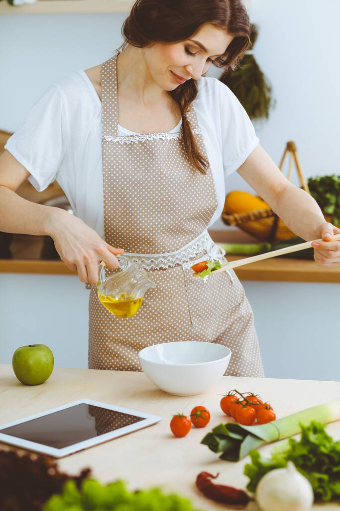 Giovane donna bruna che cucina in cucina. Casalinga che tiene in mano un cucchiaio di legno. Concetto alimentare e sanitario - Foto, immagini
