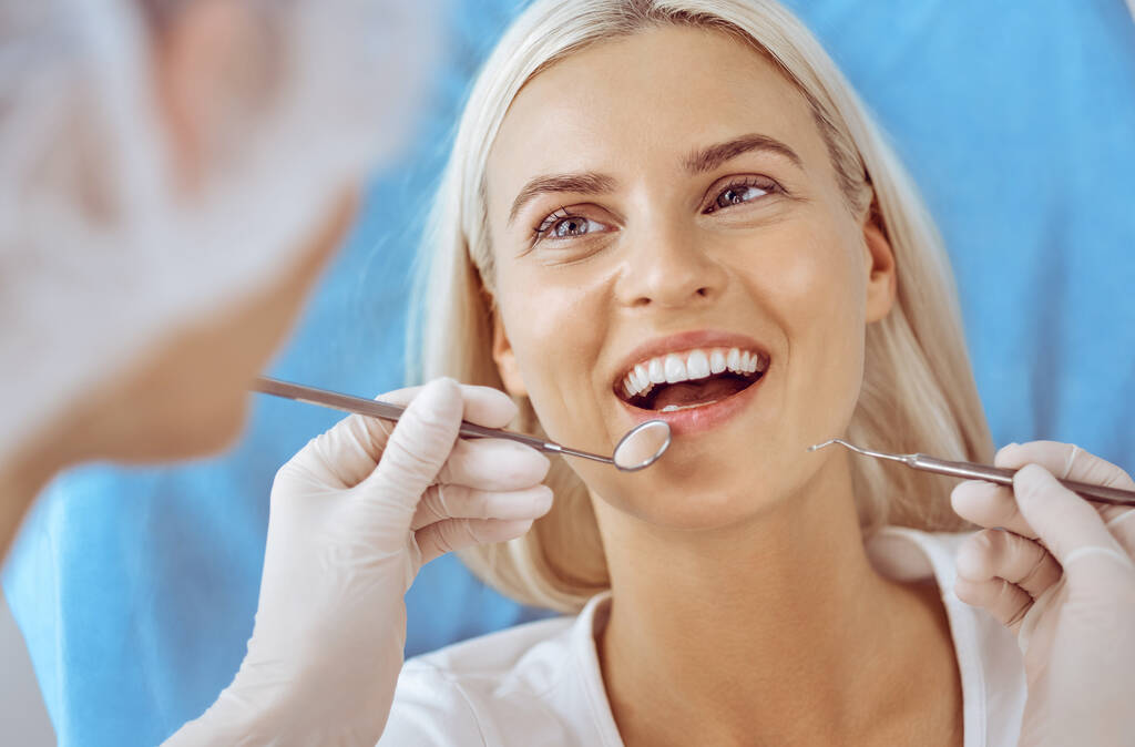 Lächelnde blonde Frau, die vom Zahnarzt in der Zahnklinik untersucht wird. Gesunde Zähne und medizinisches Konzept - Foto, Bild
