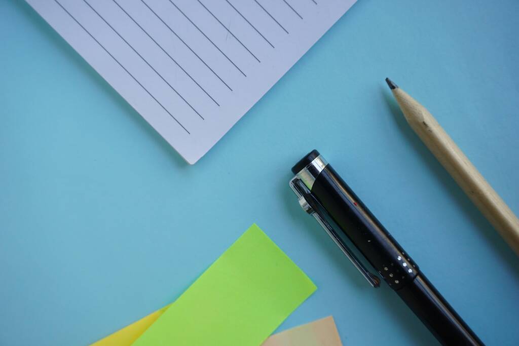 Ένας ψηλός άγγελος πυροβόλησε ένα μολύβι στυλό σημειωματάριο και χρωματιστό σημείωμα κενό στο μπλε τραπέζι - Φωτογραφία, εικόνα