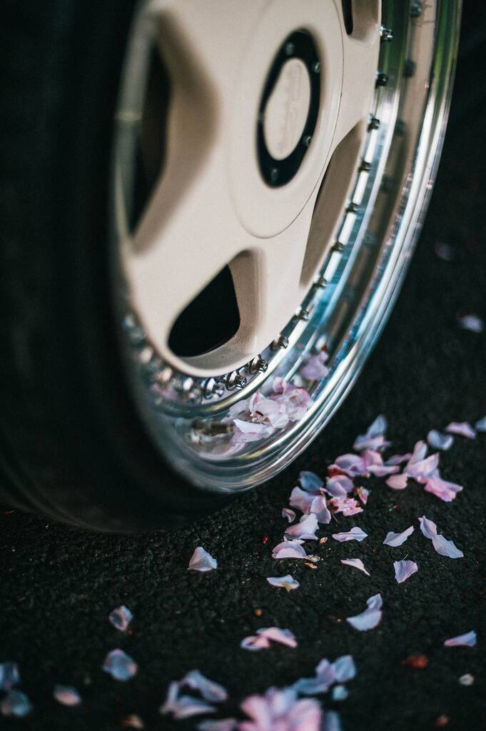 Un primo piano di una ruota auto con piccoli petali di fiori rosa che lo circondano - Foto, immagini