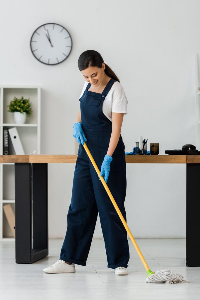 Usmívající se čistič v gumových rukavicích mytí podlahy s mop v kanceláři  - Fotografie, Obrázek