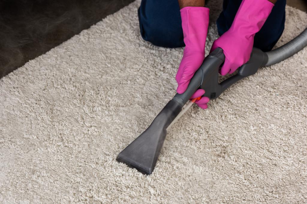 Vue recadrée du nettoyeur afro-américain utilisant un aspirateur tout en nettoyant le tapis à la maison  - Photo, image