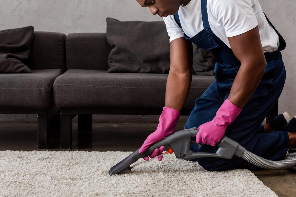 Vista recortada del limpiador afroamericano utilizando aspiradora en la alfombra en la sala de estar
 - Foto, Imagen