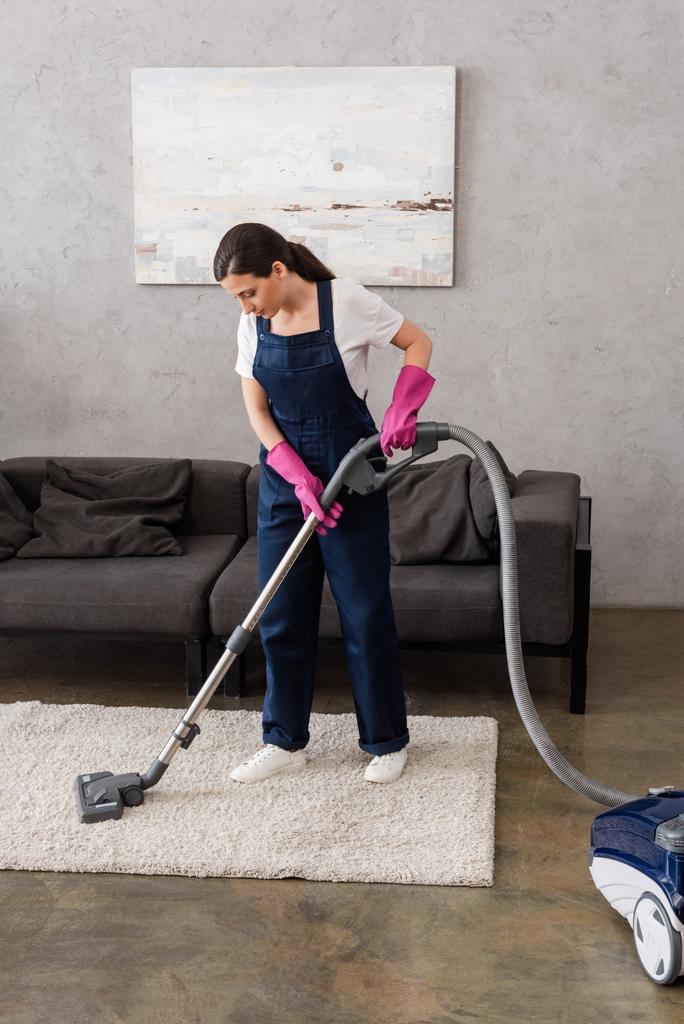 Aantrekkelijke reiniger in uniform stofzuigen tapijt in de woonkamer - Foto, afbeelding