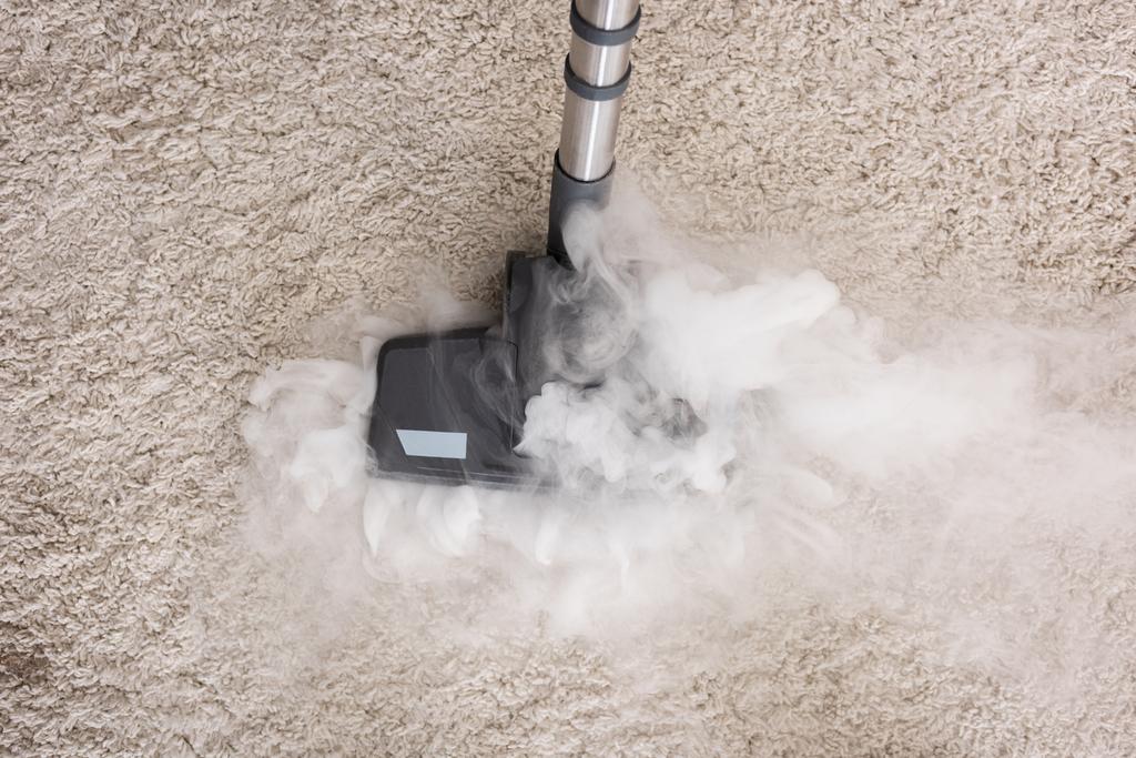 Draufsicht auf Staubsaugerbürste mit heißem Dampf auf Teppich zu Hause  - Foto, Bild