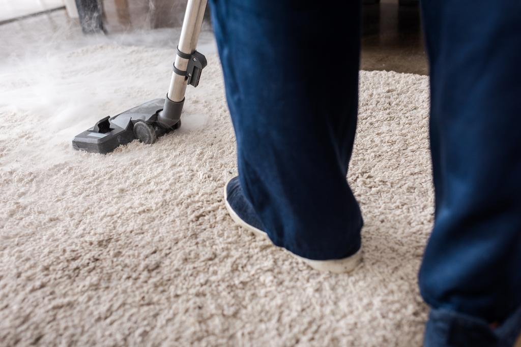 Vista cortada de limpador usando aspirador de pó com vapor quente no tapete na sala de estar
 - Foto, Imagem