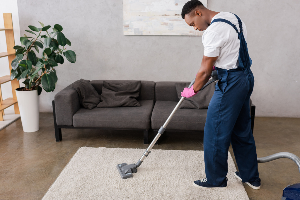 Afričtí američtí čističi v kombinézách a gumové rukavice čistící koberec při práci v obývacím pokoji - Fotografie, Obrázek