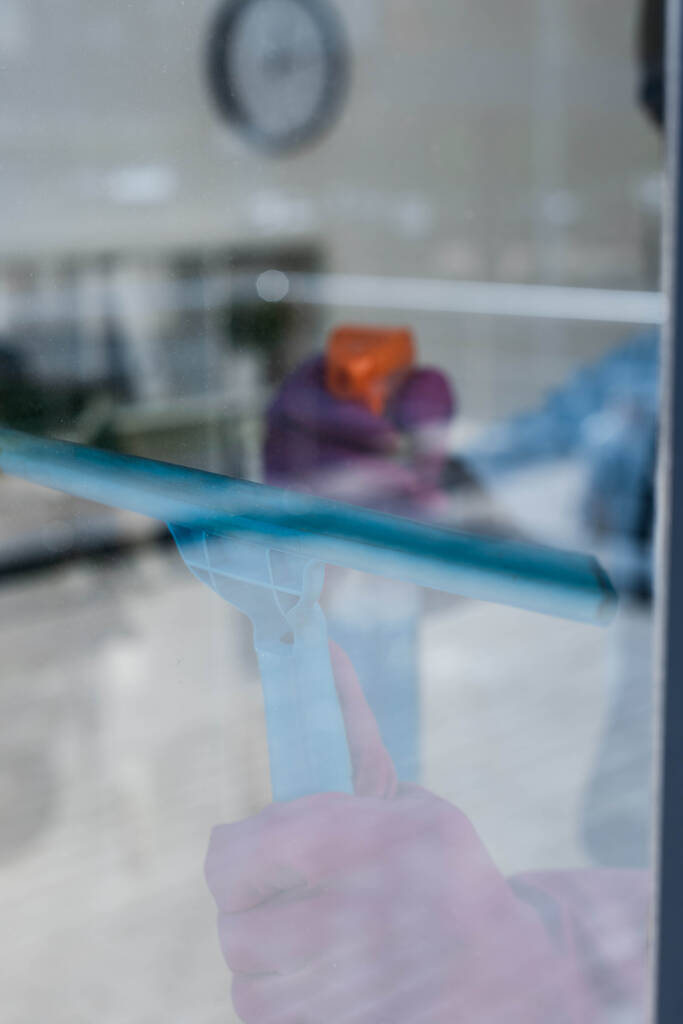 Selective focus of cleaner using squeegee handle and detergent while cleaning window in office  - Photo, Image