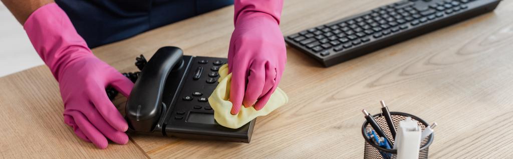 Récolte panoramique de nettoyant afro-américain dans des gants en caoutchouc nettoyage téléphone chiffon d'esprit dans le bureau  - Photo, image