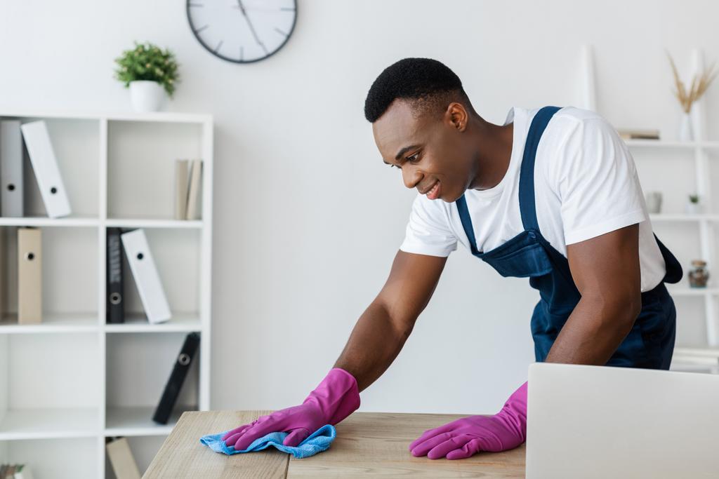 Afrikkalainen amerikkalainen siivooja siivouspöytä työskennellessään toimistossa  - Valokuva, kuva