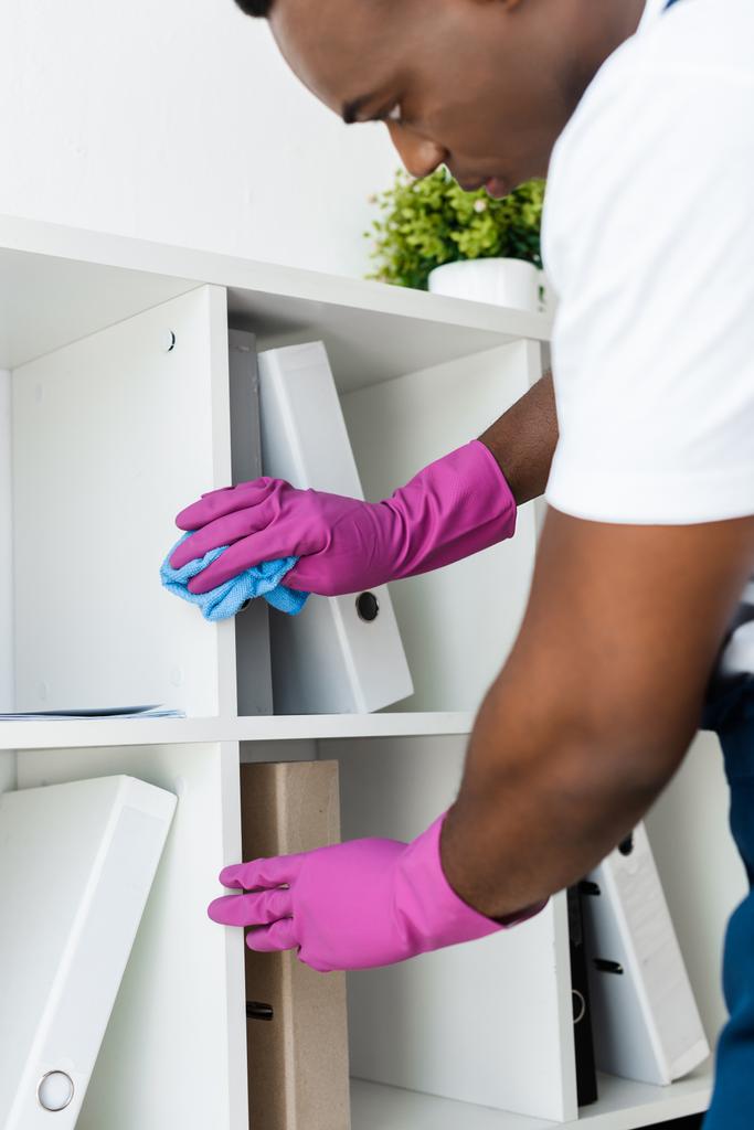 Enfoque selectivo de limpiador afroamericano en guantes de goma armario de limpieza cerca de carpetas de papel en la oficina
  - Foto, imagen