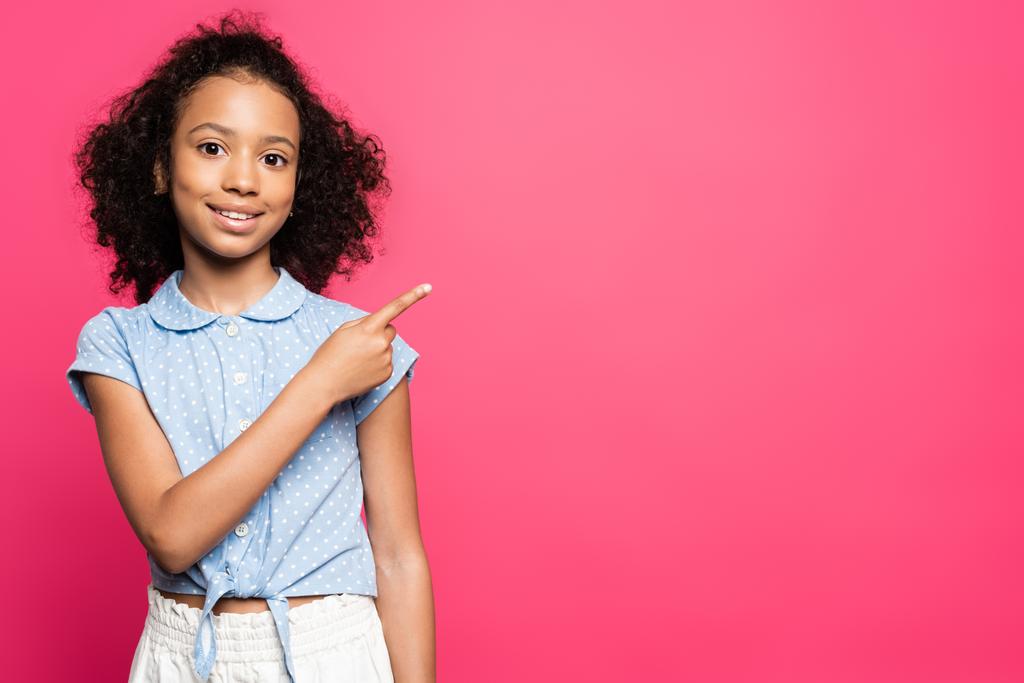 smiling cute curly african american kid pointing with finger aside isolated on pink - Photo, Image