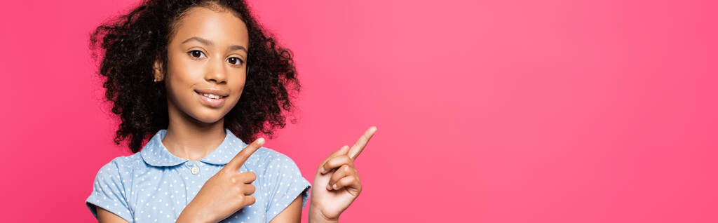 усміхнена мила кучерява афроамериканська дитина вказує пальцями в сторону ізольована на рожевому, панорамному пострілі
 - Фото, зображення