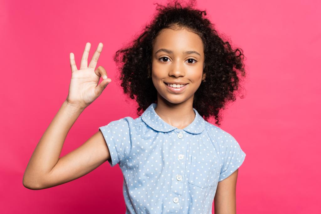 χαμογελαστό χαριτωμένο σγουρό αφροαμερικανό παιδί δείχνει ok σημάδι απομονώνονται σε ροζ - Φωτογραφία, εικόνα