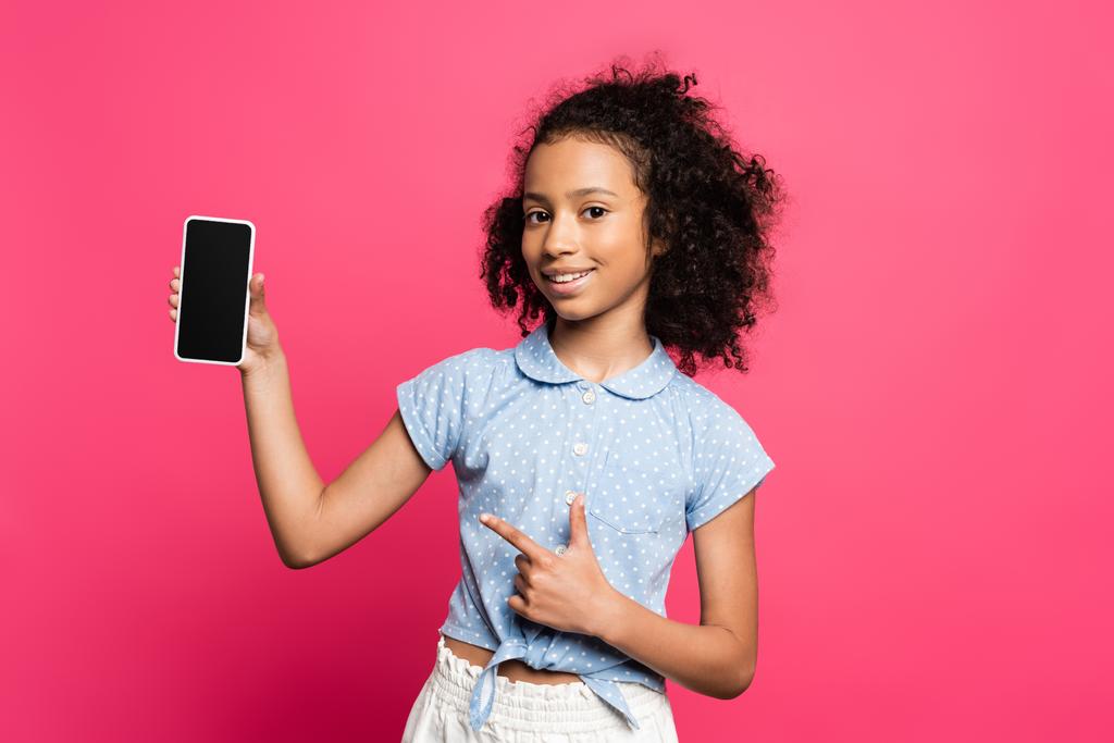 χαμογελαστή σγουρά αφροαμερικανός παιδί που δείχνει το smartphone απομονώνονται σε ροζ - Φωτογραφία, εικόνα