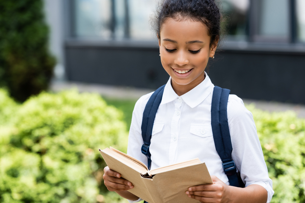 glimlachen Afrikaans amerikaans schoolmeisje voorlezen boek buiten - Foto, afbeelding