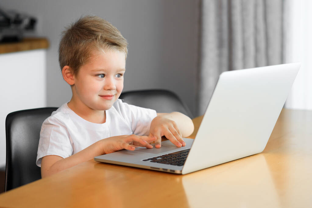 Egy fiatal fiú laptoppal ül egy asztal tetején otthon. - Fotó, kép
