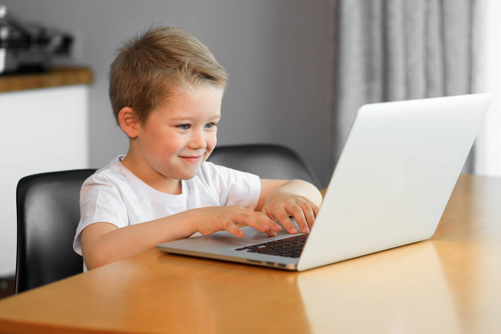 Смішний молодий хлопчик, використовуючи портативний комп'ютер, сидить на столі вдома
 - Фото, зображення