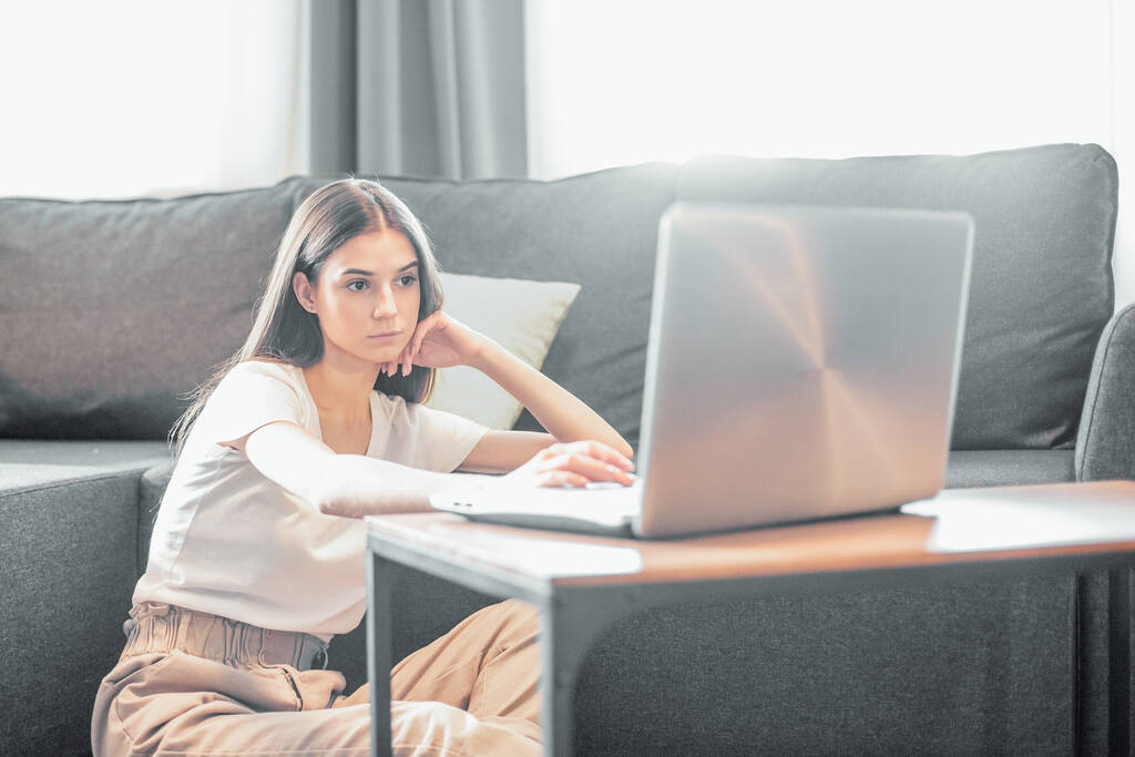 Jeune femme avec ordinateur portable moderne assis sur le canapé à la maison. Fille heureuse naviguant à travers l'Internet pendant le temps libre..  - Photo, image