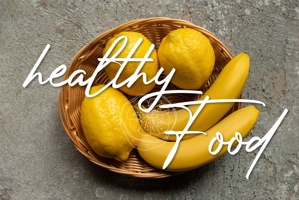 灰色のコンクリート表面のウィッカーバスケットのカラフルなバナナとレモンのトップビュー、健康的な食べ物のイラスト - 写真・画像