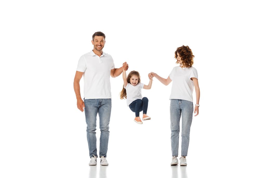 Ευτυχισμένοι γονείς κρατώντας τα χέρια της χαριτωμένης κόρης πηδώντας στα λευκά  - Φωτογραφία, εικόνα