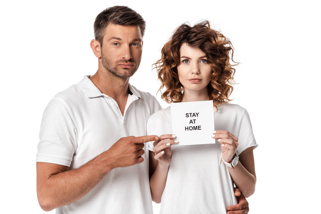 bel homme pointant avec le doigt à la carte avec rester à la maison lettrage près de femme attrayante isolé sur blanc  - Photo, image