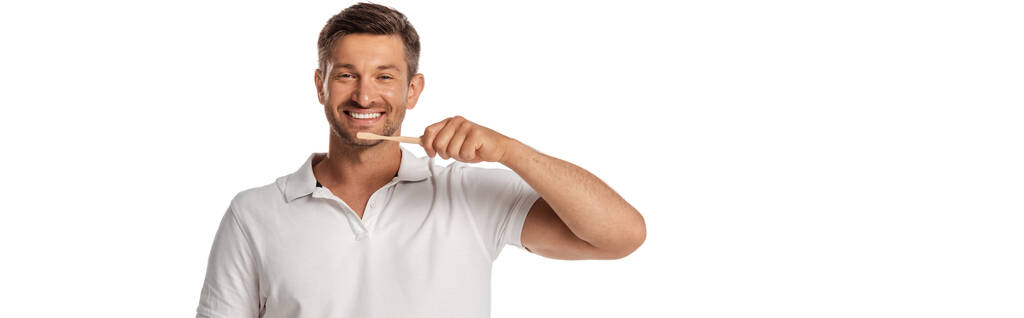 panoramiczna orientacja wesołego człowieka trzymającego szczoteczkę do zębów podczas mycia zębów odizolowanych na biało  - Zdjęcie, obraz