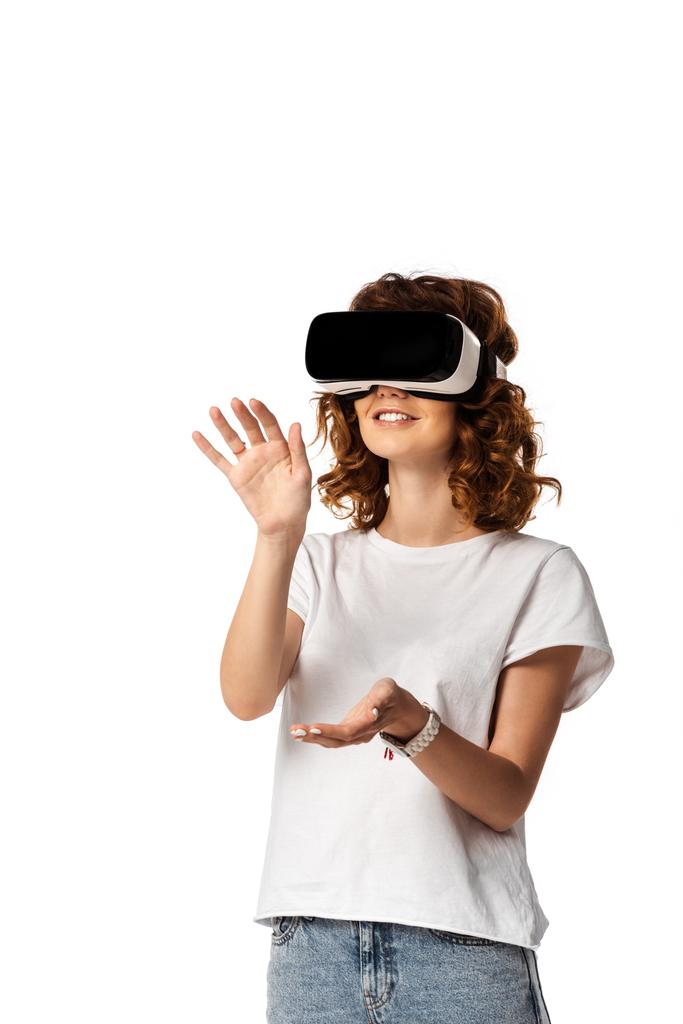 Ευτυχισμένη νεαρή γυναίκα σε εικονική πραγματικότητα ακουστικά gesturing απομονώνονται σε λευκό  - Φωτογραφία, εικόνα