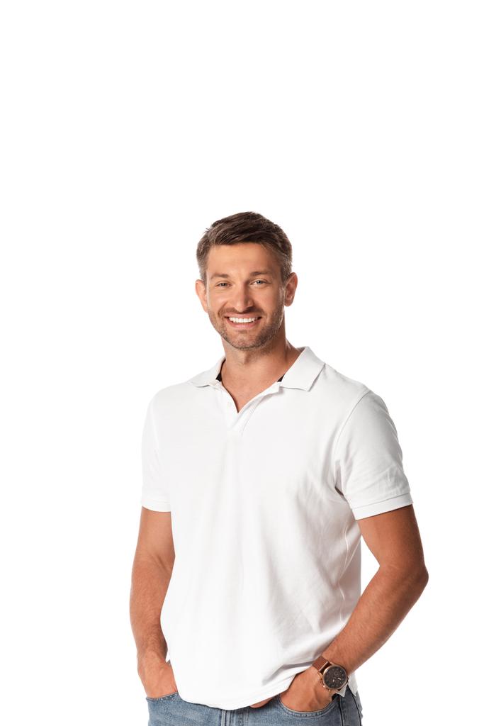 Beyaz tişörtlü neşeli bir adam gülümserken elleri ceplerinde beyazların üzerinde dikiliyor.  - Fotoğraf, Görsel