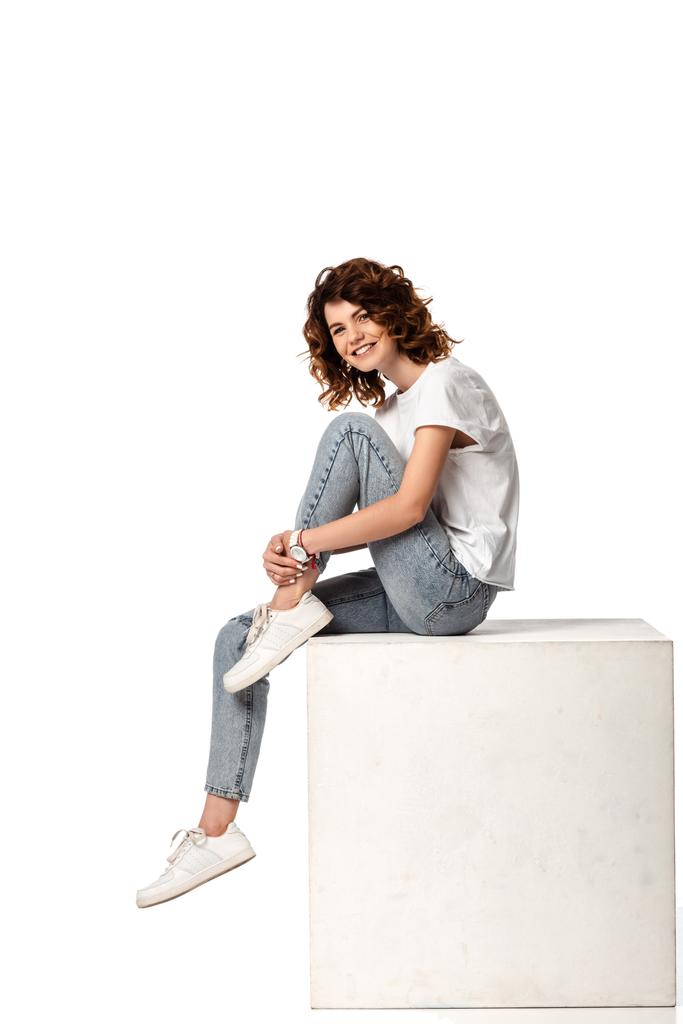 キューブの上に座って白い笑顔でいるジーンズの魅力的な女性  - 写真・画像