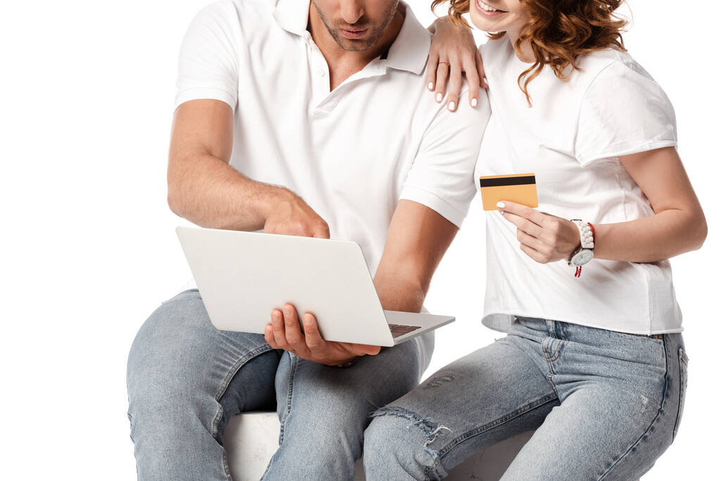 vista ritagliata di donna felice in possesso di carta di credito vicino all'uomo con computer portatile isolato su bianco - Foto, immagini