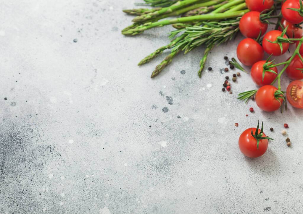 Light food background with asparagus, cherry tomatoes and rosemary on light background. Space for text - Photo, Image