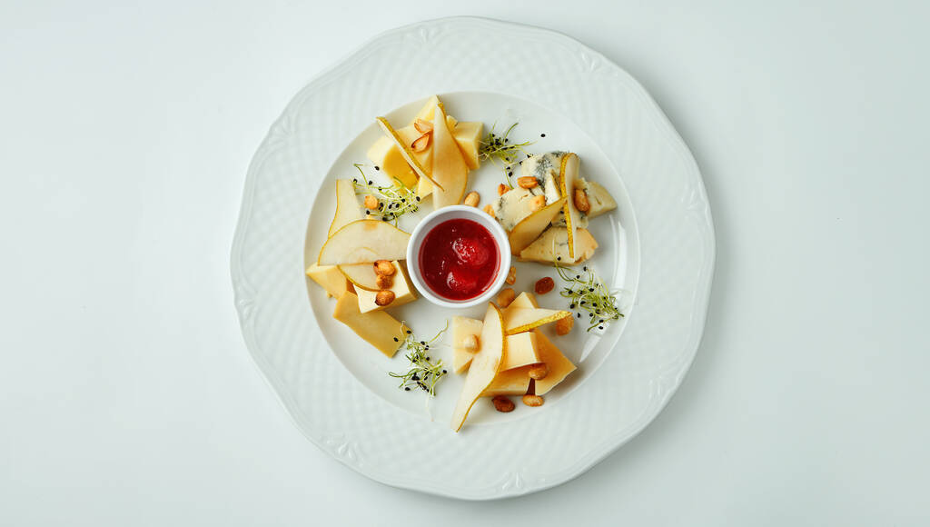 Chiudere su piatto di formaggio servito con noci, uva, miele. Vista dall'alto su diversi tipi di formaggio su sfondo bianco con spazio di copia. - Foto, immagini