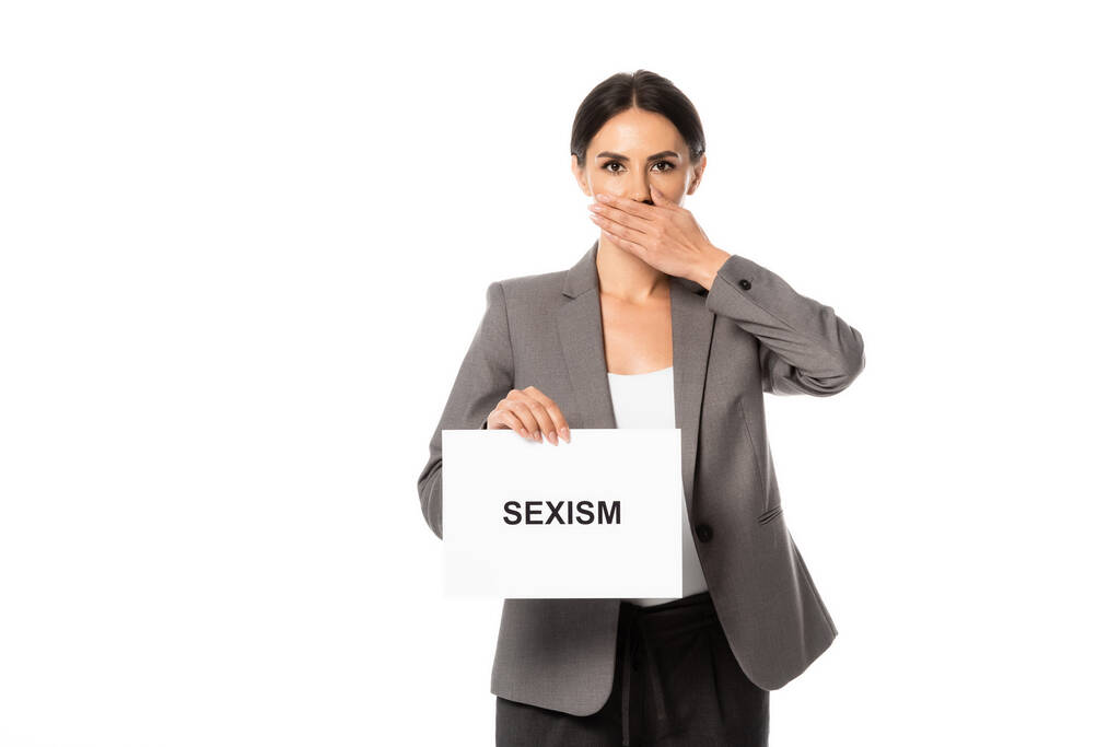 empresária cobrindo boca enquanto segurando cartaz com sexismo lettering isolado no branco
 - Foto, Imagem