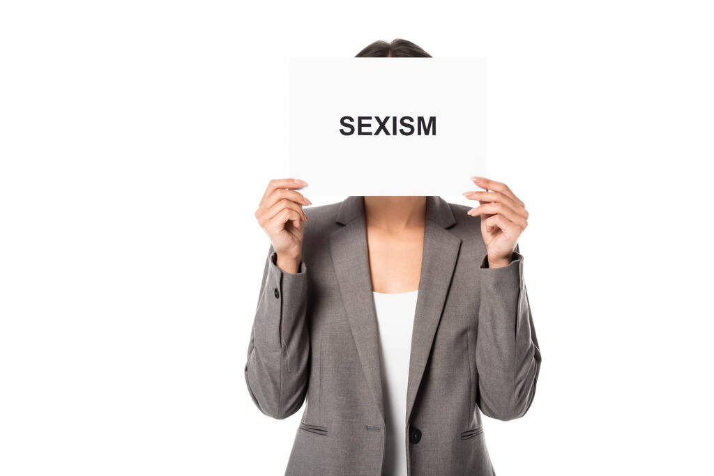 femme d'affaires couvrant le visage tout en tenant une pancarte avec lettrage sexisme isolé sur blanc - Photo, image