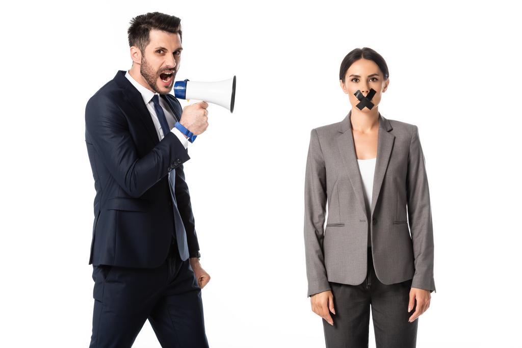 bebaarde zakenman schreeuwt in megafoon in de buurt van zakenvrouw met duct tape op de mond geïsoleerd op wit, genderongelijkheid concept  - Foto, afbeelding