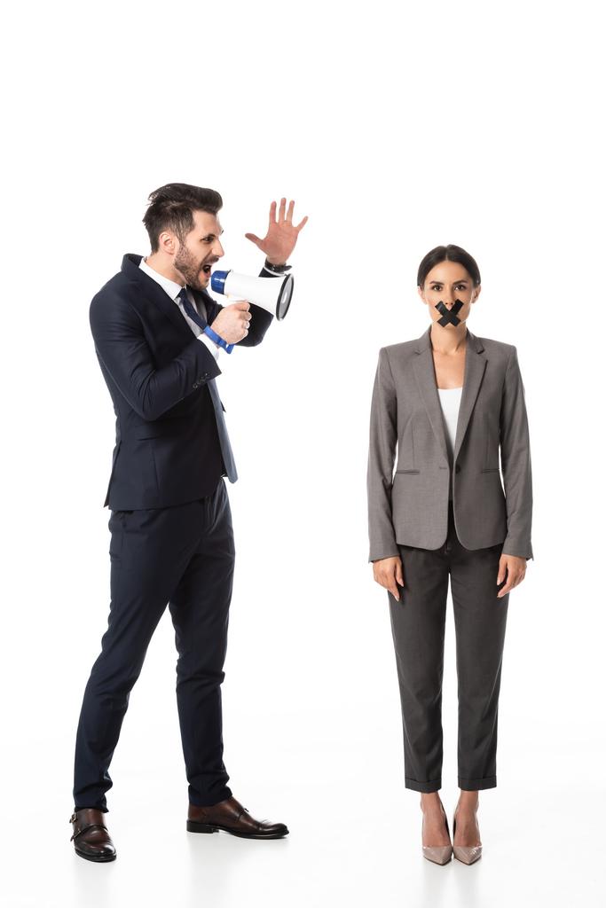 bearded businessman screaming in megaphone and gesturing near businesswoman with duct tape on mouth on white - Photo, Image