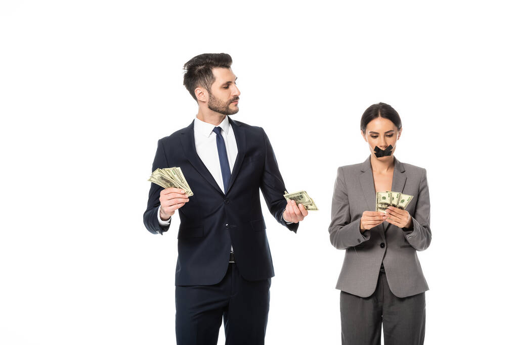 homme d'affaires tenant des dollars et regardant femme d'affaires avec du ruban adhésif sur la bouche isolé sur blanc, concept d'inégalité des sexes - Photo, image