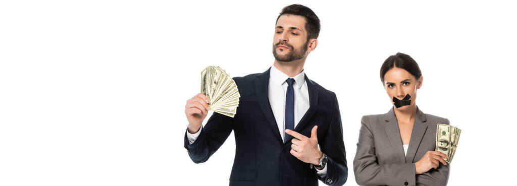 horizontal image of man pointing with finger at dollars near businesswoman with duct tape on mouth standing with crossed arms isolated on white - Photo, Image