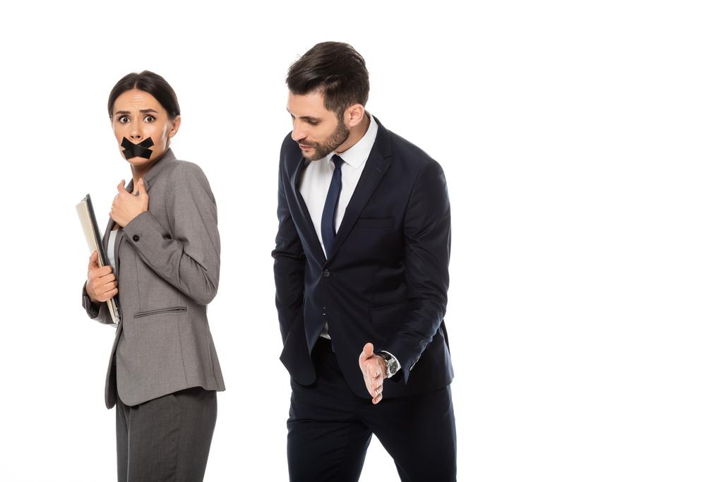 zakenman in formele slijtage molesteren zakenvrouw met scotch tape op de mond geïsoleerd op witte, seksuele intimidatie concept   - Foto, afbeelding