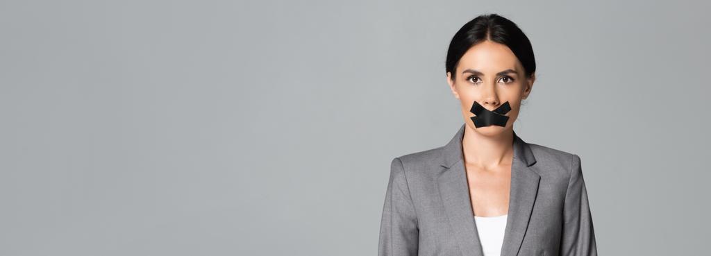 panoramische Orientierung der Geschäftsfrau mit Klebeband auf dem Mund isoliert auf grau - Foto, Bild