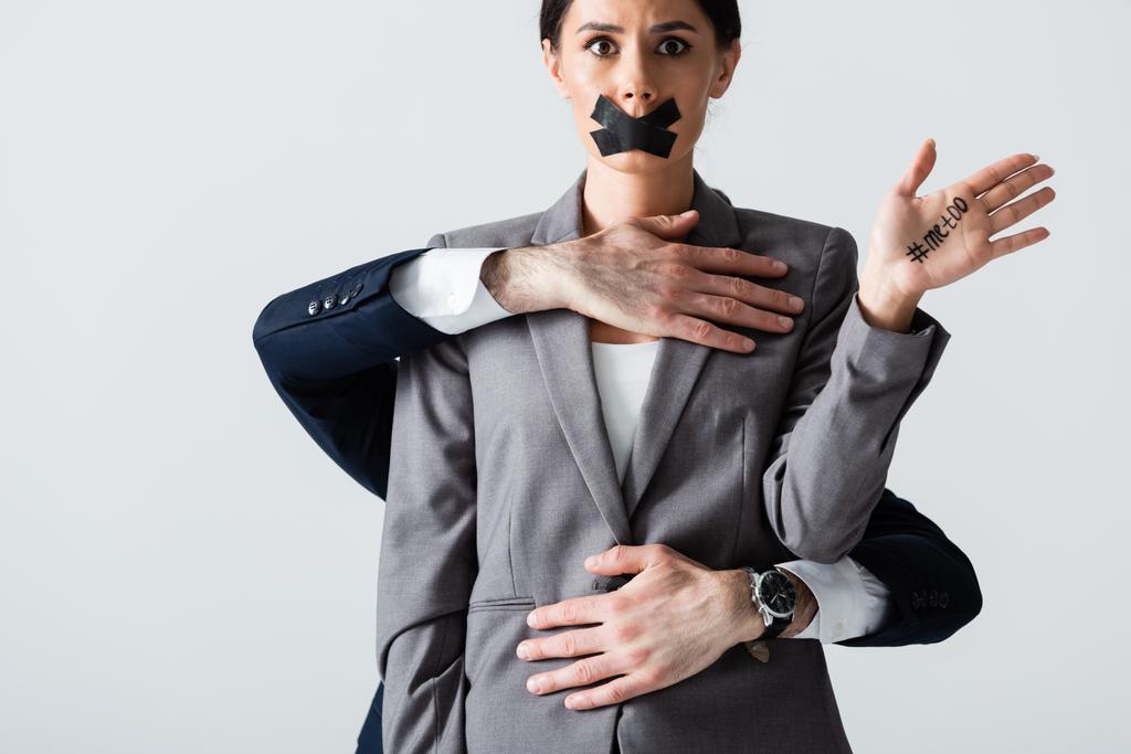 Geschäftsmann belästigt Geschäftsfrau mit Klebeband auf dem Mund zeigt Hand mit mir zu Schriftzug isoliert auf weiß - Foto, Bild