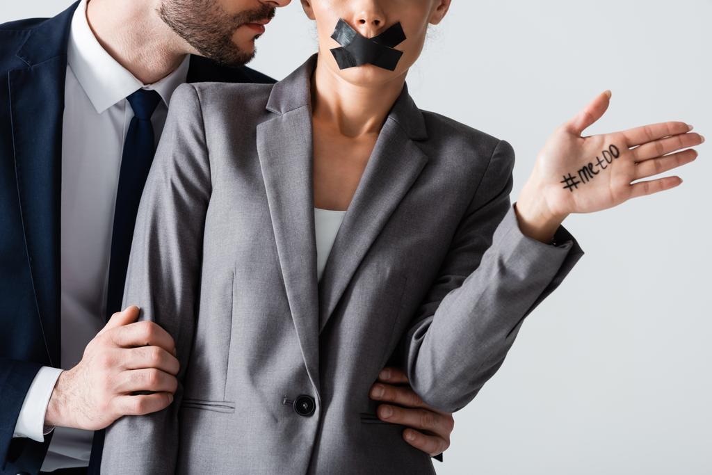 abgeschnittene Ansicht von Geschäftsmann belästigt Geschäftsfrau mit Klebeband auf dem Mund zeigt Hand mit mir zu Schriftzug isoliert auf weiß - Foto, Bild